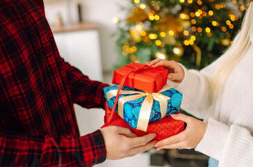 Wall Mural - Beautiful couple in love near the Christmas tree, celebrating the exchange of gifts, spending time together. Holiday concept.