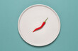 One chili pepper on a beige plate, turquoise background. Creative layout. Top view, flat lay.