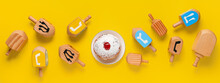 Many Dreidels And Tasty Donut For Hanukkah Celebration On Yellow Background, Top View