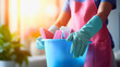 Cleaning lady wearing pink apron and blue gloves, holding the bucket full of equipment for house cleaning, blurred background