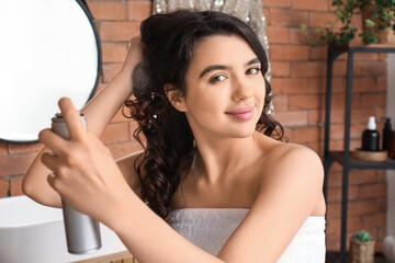 Poster - Pretty young woman applying hair spray on her curly hair in bathroom