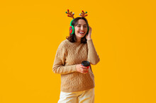 Young Woman In Reindeer Horns With Cup Of Coffee On Yellow Background