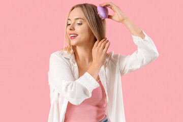 Wall Mural - Young blonde woman brushing hair on pink background