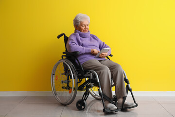 Poster - Senior woman in wheelchair using tablet computer near yellow wall