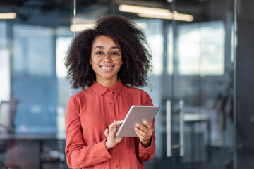 Portrait young successful businesswoman with tablet computer in hands inside office at workplace, female programmer testing new software smiling looking at camera satisfied with achievement results.