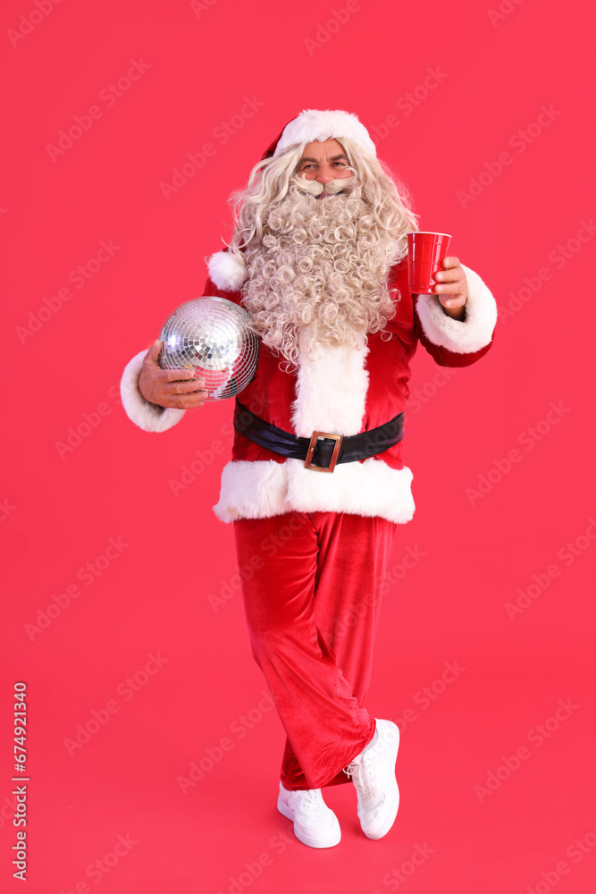Santa Claus with disco ball and cup on red background