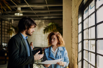 Wall Mural - Young businesswoman reading document with colleague in office