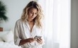 © piai - A woman in shirt looking at mobile phone in bright bedroom