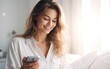© piai - A woman in shirt looking at mobile phone in bright bedroom