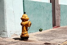 A Yellow Fire Hydrant In Stark Contrast To The Muted Blue-bricked Building Behind It, Puerto Rico