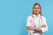 Doctor with pink ribbon and stethoscope on light blue background, space for text. Breast cancer awareness