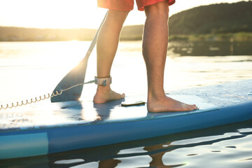 Wall Mural - Man paddle boarding on SUP board in river at sunset, closeup