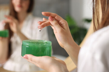 Poster - Young woman holding jar of aloe hair mask near mirror indoors, closeup