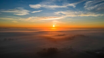 Poster - Aerial view of breathtaking landscape of the sun setting behind a rolling blanket of fog