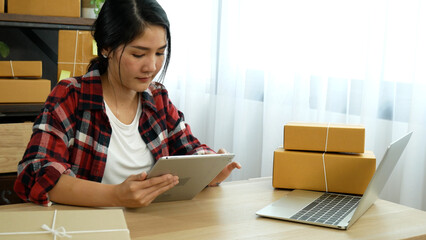 Woman checking stock goods supply delivery package shipping use document checklist. Asian woman startup small business at home office. Online entrepreneur asian woman use tablet checking online order