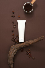 White plastic tube with facial cleanser or mask displayed on brown background with coffee beans, coffee powder and dry twig. Mockup tube for design, concept for advertising organic cosmetic