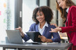 © amnaj - Two happy businesswoman talking and consulting working together in the office. Businesswoman discussing with colleague over laptop at desk in office.