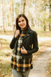 © Mila - A beautiful girl in jeans and a plaid shirt walks in a birch grove. Portraits of a brunette girl in nature, in the autumn forest