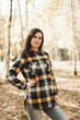 © Mila - A beautiful girl in jeans and a plaid shirt walks in a birch grove. Portraits of a brunette girl in nature, in the autumn forest