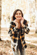 © Mila - A beautiful girl in jeans and a plaid shirt walks in a birch grove. Portraits of a brunette girl in nature, in the autumn forest