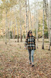 © Mila - A beautiful girl in jeans and a plaid shirt walks in a birch grove. Portraits of a brunette girl in nature, in the autumn forest