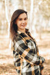© Mila - A beautiful girl in jeans and a plaid shirt walks in a birch grove. Portraits of a brunette girl in nature, in the autumn forest