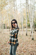 © Mila - A beautiful girl in jeans and a plaid shirt walks in a birch grove. Portraits of a brunette girl in nature, in the autumn forest