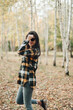 © Mila - A beautiful girl in jeans and a plaid shirt walks in a birch grove. Portraits of a brunette girl in nature, in the autumn forest