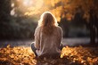 Mujer rubia sentada en el suelo. Está en un parque con árboles en otoño. Da la sensación de que está mirando su telefono móvil