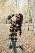 © Mila - A beautiful girl in jeans and a plaid shirt walks in a birch grove. Portraits of a brunette girl in nature, in the autumn forest
