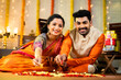 © WESTOCK - Happy indian couple in traditional wear looking camera while decorating rangoli with flower for festival celebration on floor - concept of religious custom, bonding, and religious ceremony.