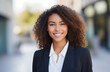 © Anzhela - Classy smiling young businesswoman in suit voluminous curly hair wearing on city street background