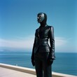 A person wearing all black leather costume standing on the seashore. Black latex suit, leather gloves and face mask. Latex clothes. Weird look. Fetish. Sub. Domination. Submissive