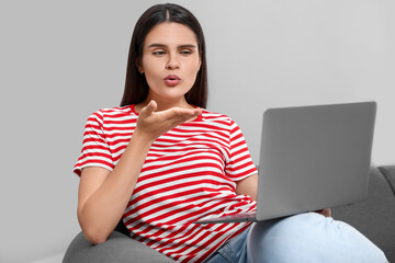 Poster - Young woman having video chat via laptop and blowing kiss on sofa in room