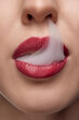 © Lustre Art Group  - Cropped photo. Extreme close up of woman with red lips blowing smoke from mouth. Bad habits. No smoking or quit smoking.