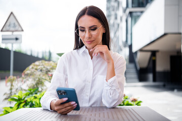 Poster - Photo of pretty positive elegant girl sit coffee table use smart phone chatting texting bright day city center outdoors