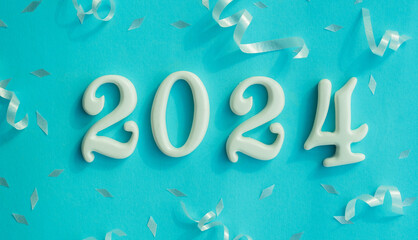 Wall Mural - close up number 2024 shape wood on blue color background with rolling ribbon and confetti for happy 