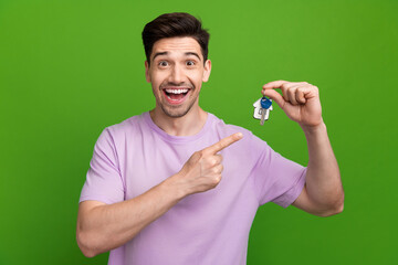 Canvas Print - Photo of impressed excited man with brunet hair dressed purple t-shirt directing on keys from his home isolated on green color background