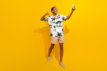 Wall Mural - Full length photo of nice young male showing thumb up selfie walk wear trendy palms print garment isolated on yellow color background