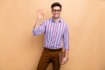 Poster - Photo of good mood office guy manager bring laptop and showing okey sign enjoying this work day isolated on beige color background