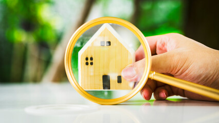 Wall Mural - Hand holding magnifying glass and looking at house model, house selection, real estate concept.