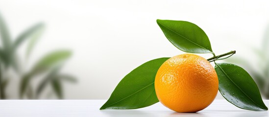 Wall Mural - The ripe orange fruit known for its vibrant color and juicy flavor rests on a white table with a green leaf in the background embodying the essence of nature and health while being isolated 