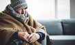 It's cold in the house in winter. A senior Person freezing, fever or trouble with heating. Sad person in wool plaid and scarf and wearing warm hat sitting on sofa at home in wintertime