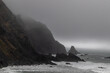 Rocks off route 101 coastal highway during a storm, Image shows the rough Pacific ocean swells hitting the cliffs and low level fog and mist covering the bay 