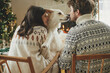 Happy young family in cozy sweaters hugging with cute dog and relaxing on background of fireplace and modern christmas tree. Merry Christmas! Pets and winter holidays