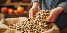 Hands With Pumpkin Seeds In Burlap Sack On Wooden Surface. Sack Full Of Nuts Prepared For Easy Snack Bag. Consuming Local Commerce In Small Businesses And Cooperatives That Produce Organic Foods.