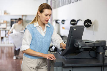 Female employee of the printing house adjusts the plotter using a computer