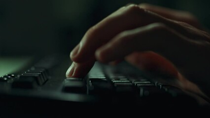 Focused hacker programmer working in a dark room, typing on the keyboard of his laptop computer. His freelance work is done in the comfort of his own home