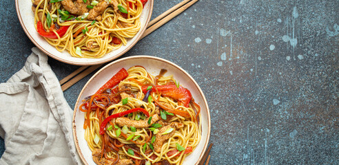 Poster - Two bowls with Chow Mein or Lo Mein, traditional Chinese stir fry noodles with meat and vegetables, served with chopsticks top view on rustic blue concrete background, space for text.