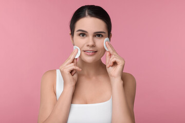 Wall Mural - Young woman cleaning her face with cotton pads on pink background